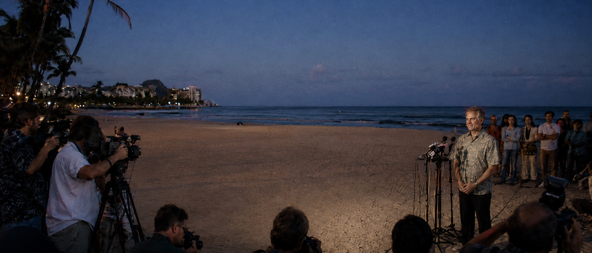 Beach press conference with cameras, microphones, reporters, and a speaker addressing media near Miami Beach.
