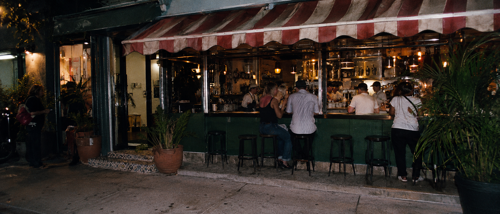 Local Coral Gables, Florida restaurant storefront at night with guests seated at a ventanita-style counter under a striped awning.